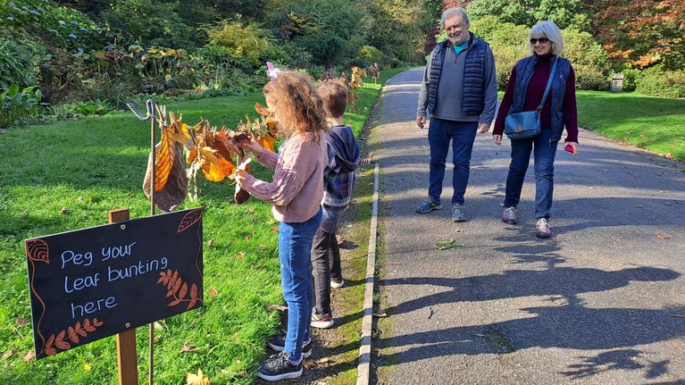 Two children hanging leaves on string in a garden with two adults nearby